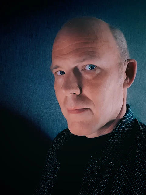 Brian Dear in a dark shirt against a teal-blue studio backdrop